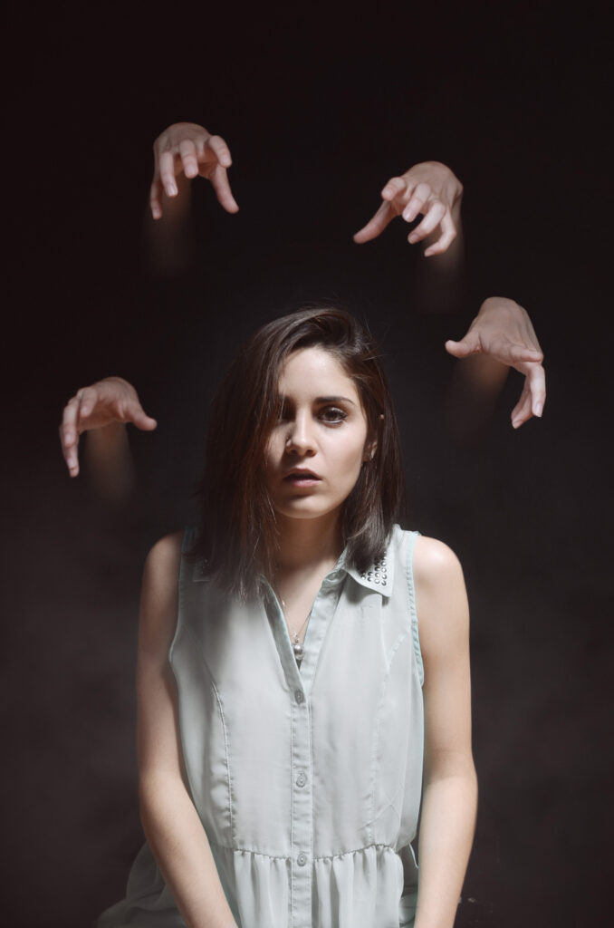 Mariana Esquivel a woman in a white sleeveless shirt surrounded by multiple hands reaching out towards her set against a dark background.